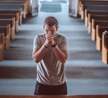 Photo of a man in prayer at the front of an empty church